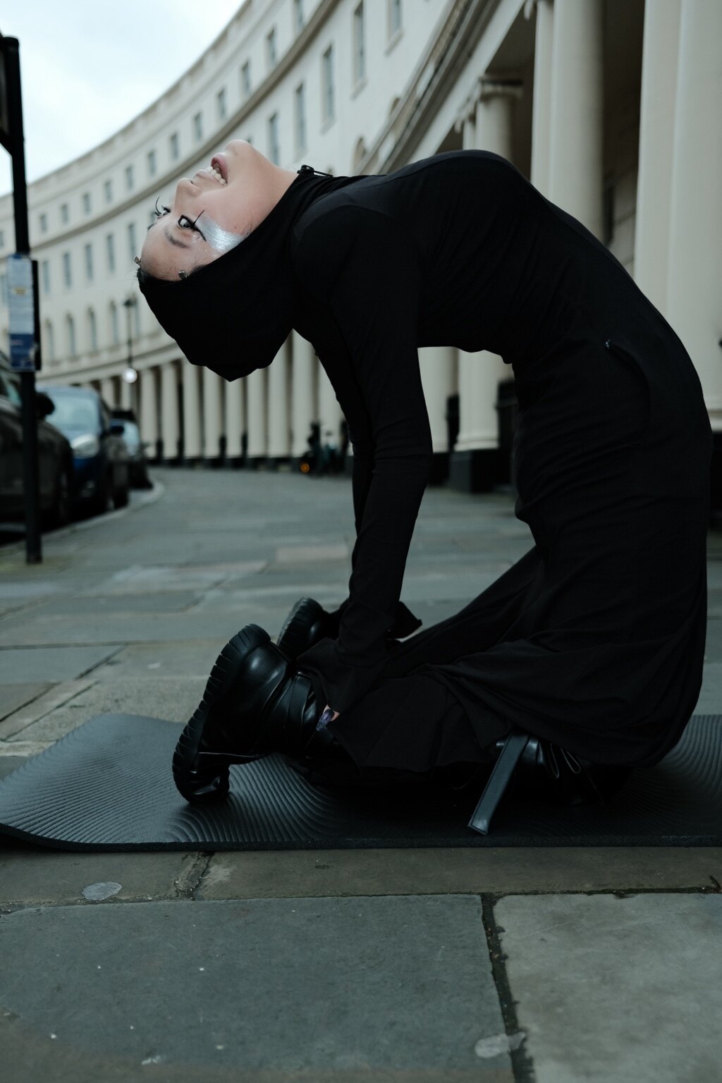 A figure performing a backbend on a yoga mat in a London street